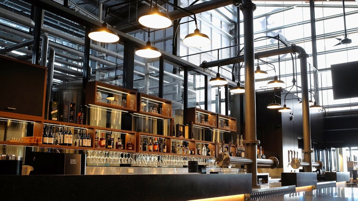 a view of the bar shelves lined with various spirits and glasses, industrial lighting overhead