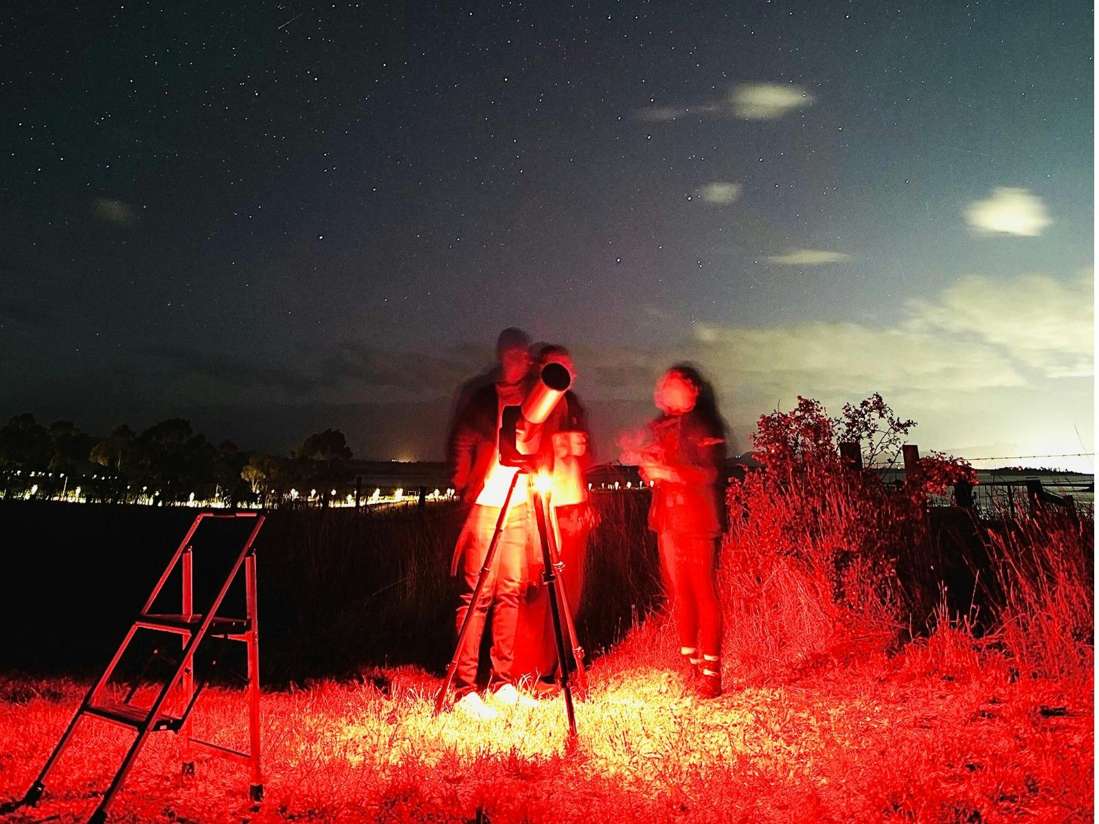 Guide showing guests the night sky while illuminated by soft red light.