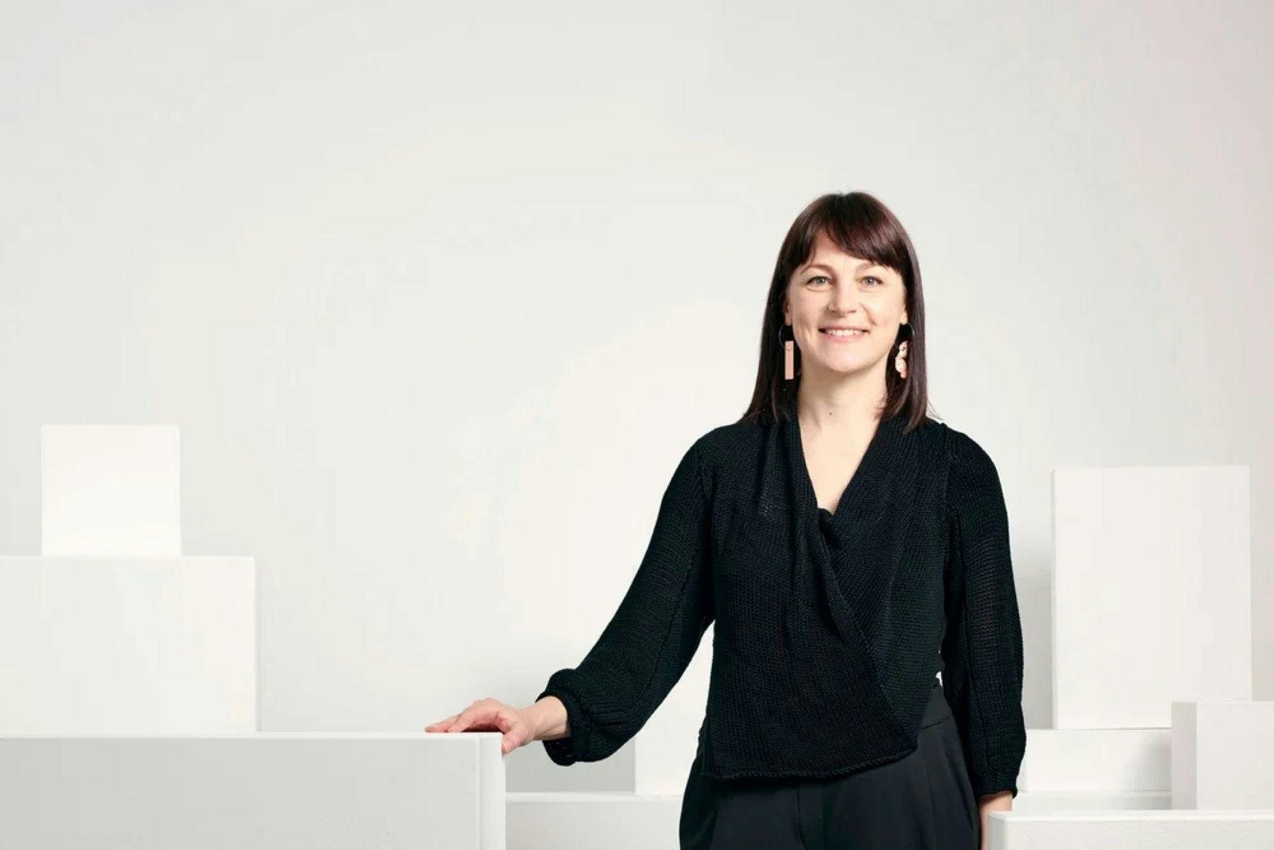 Phoebe Porter standing by white plinths and gallery wall smiling