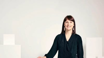 Phoebe Porter standing by white plinths and gallery wall smiling