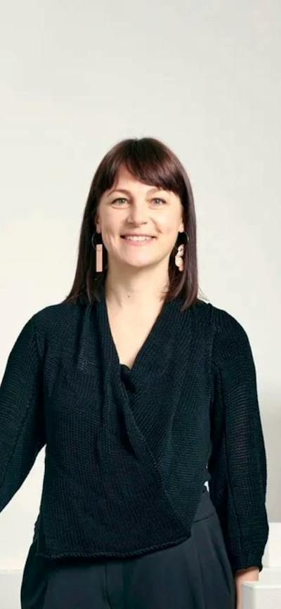 Phoebe Porter standing by white plinths and gallery wall smiling