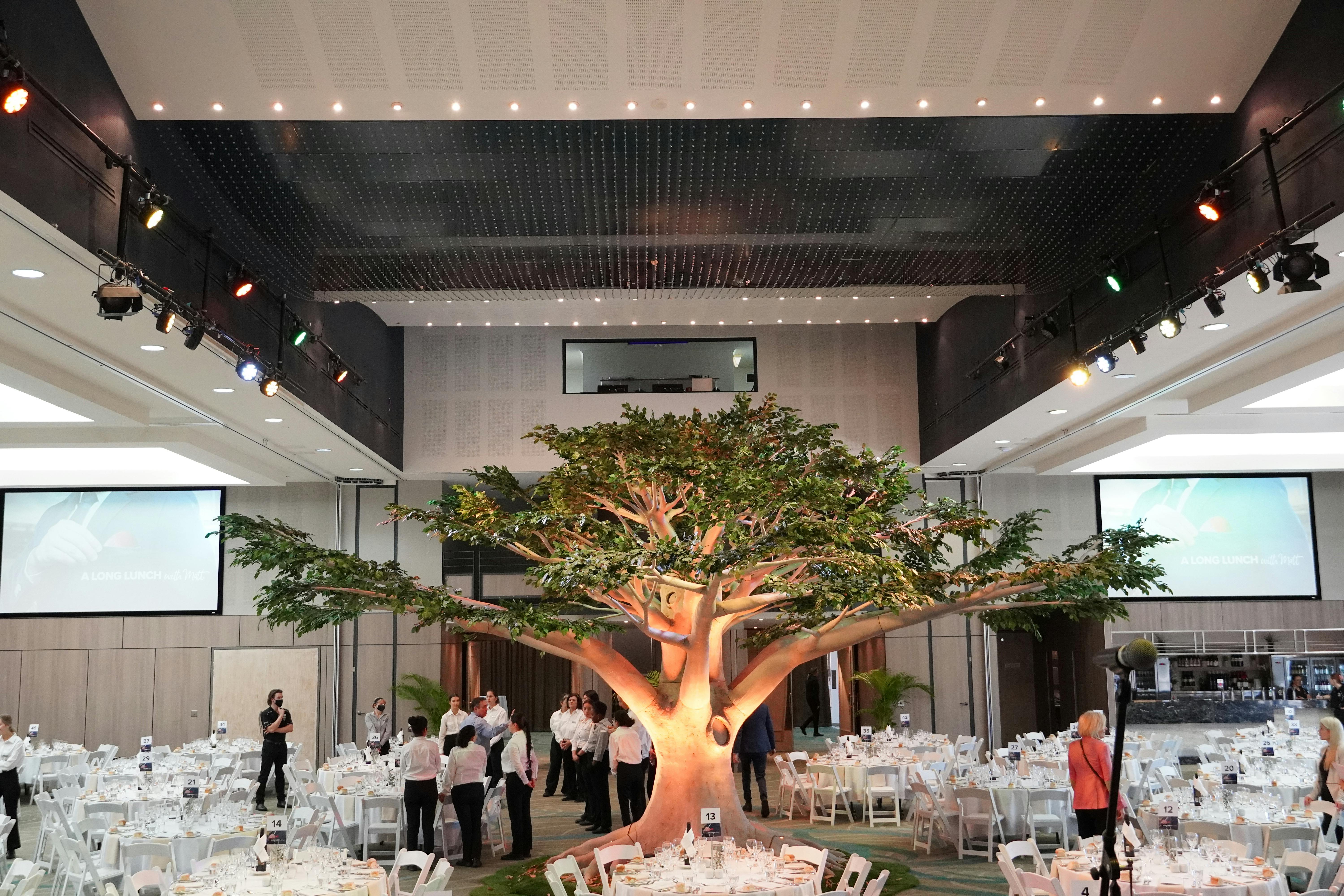 A tree installation inside a function room, with tables and chairs prepared for an event