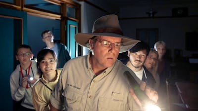 Tim holds a torch and leads a group of people through the dark halls of Old Parliament House