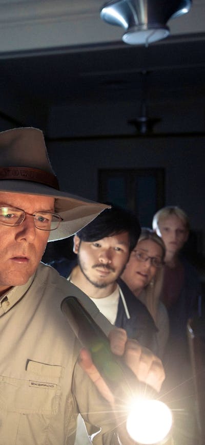 Tim holds a torch and leads a group of people through the dark halls of Old Parliament House