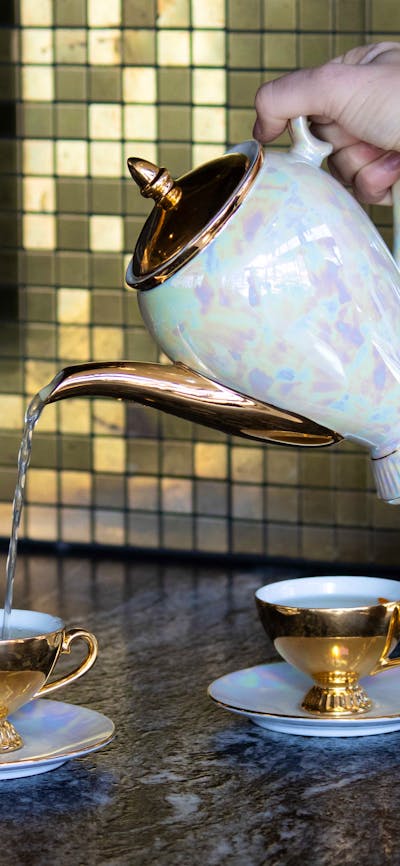 A photo of a teapot pouring a cocktail into a teacup at a bar.