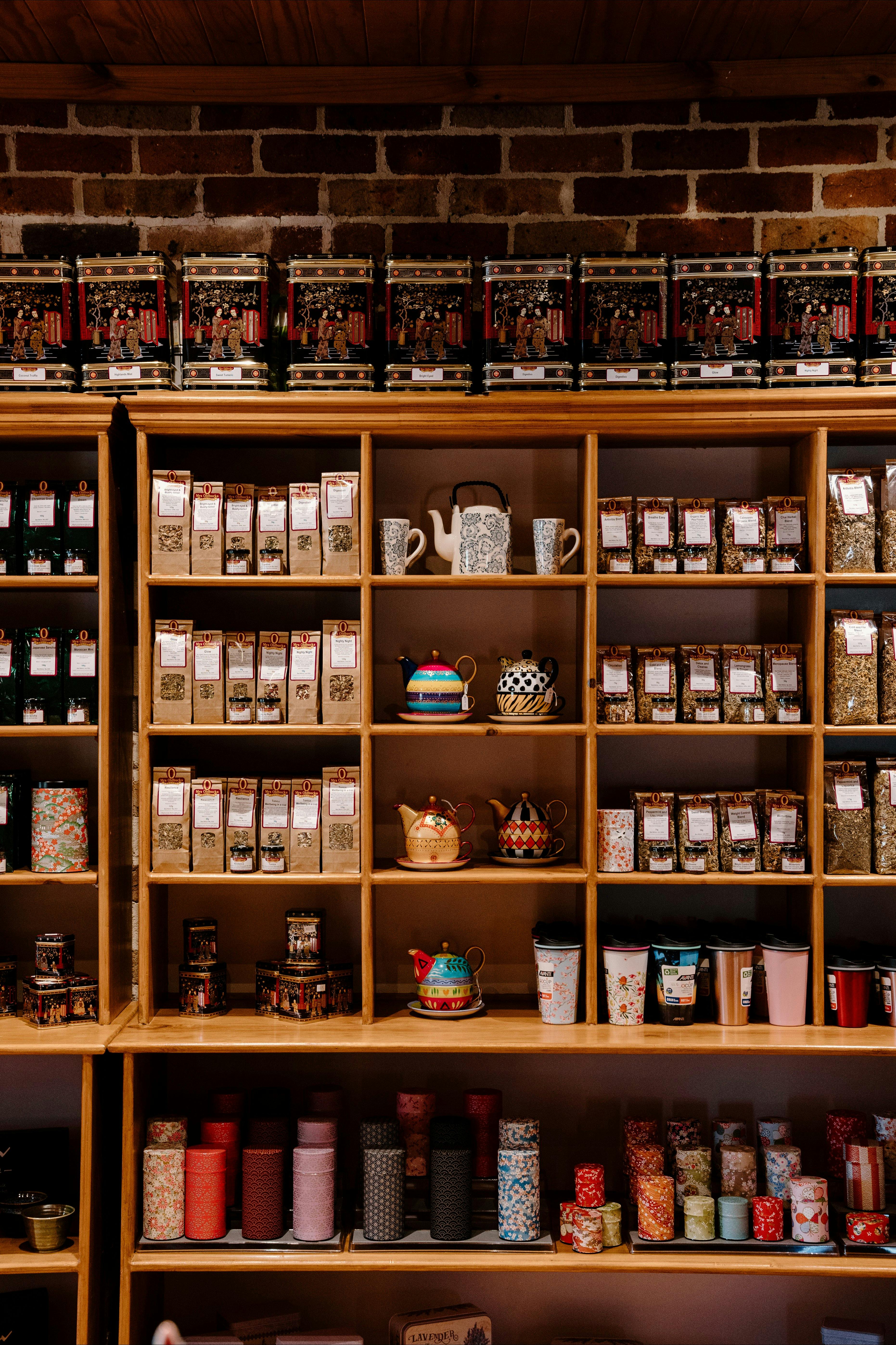 Shelves with tea tins, teapots, mugs, and packaged goods against a brick wall background