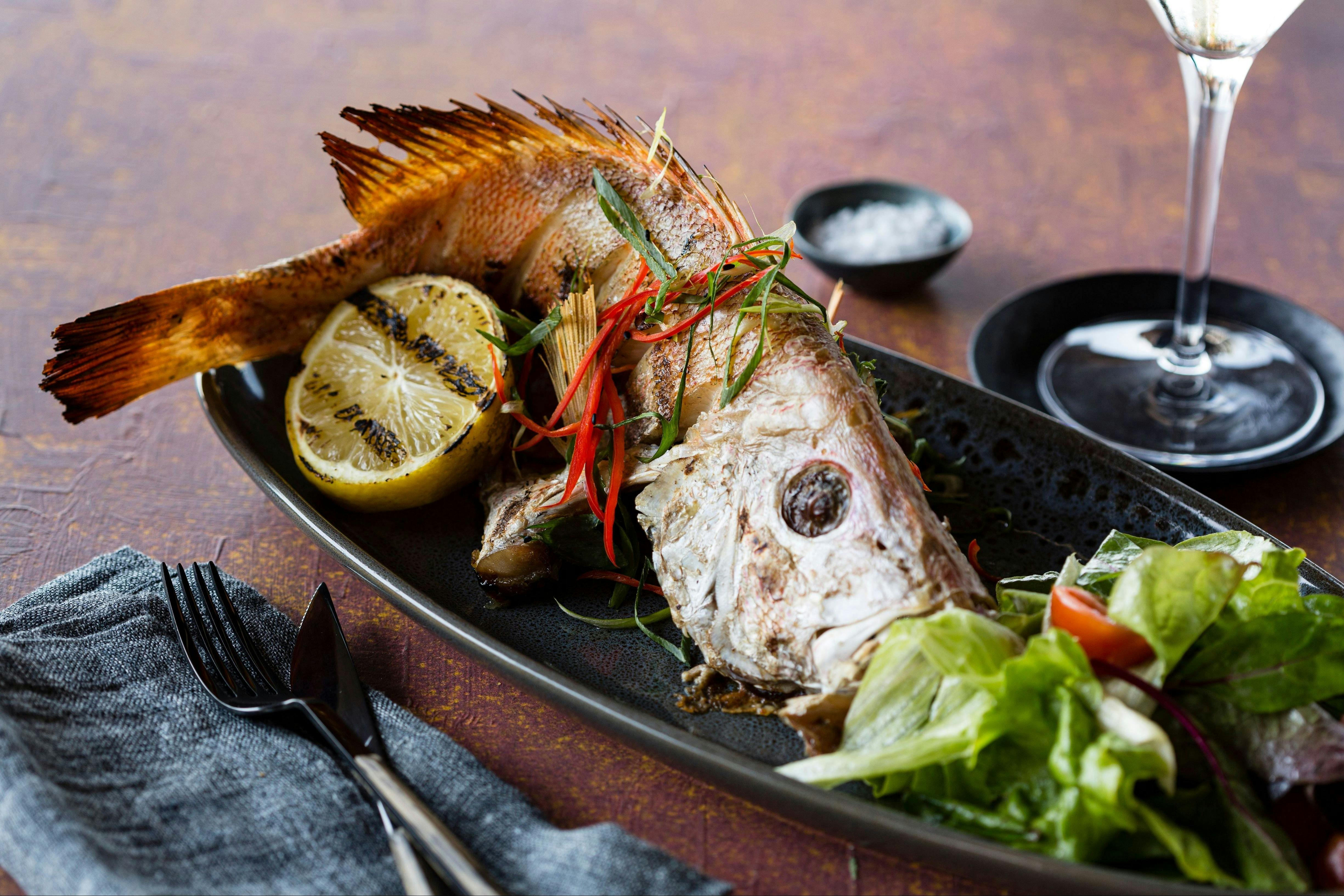 A whole roasted reef fish served with grilled lemon, chilli, fresh herbs and a side salad.