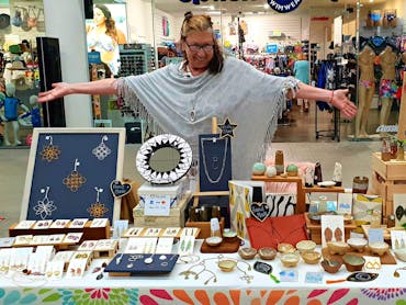 A stallholder smiling and displaying her wares at The Pier Markets