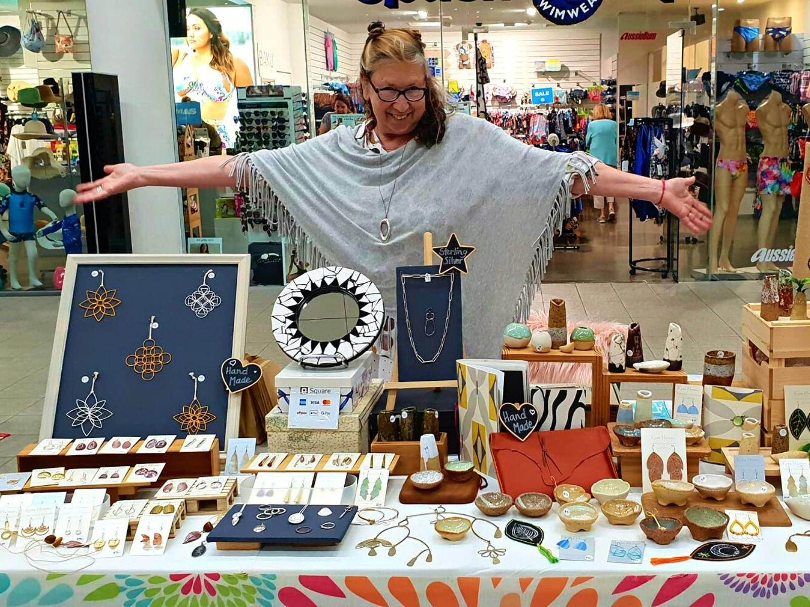 A stallholder smiling and displaying her wares at The Pier Markets A stallholder smiling and displaying her wares at The Pier Markets
