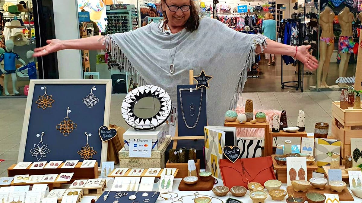 A stallholder smiling and displaying her wares at The Pier Markets