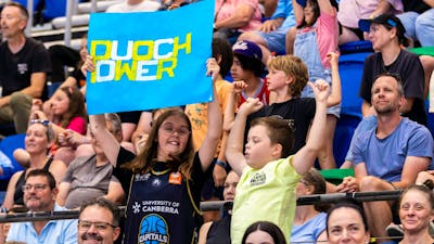 Two young fans cheering in the stands while waving a UC Capitals poster.