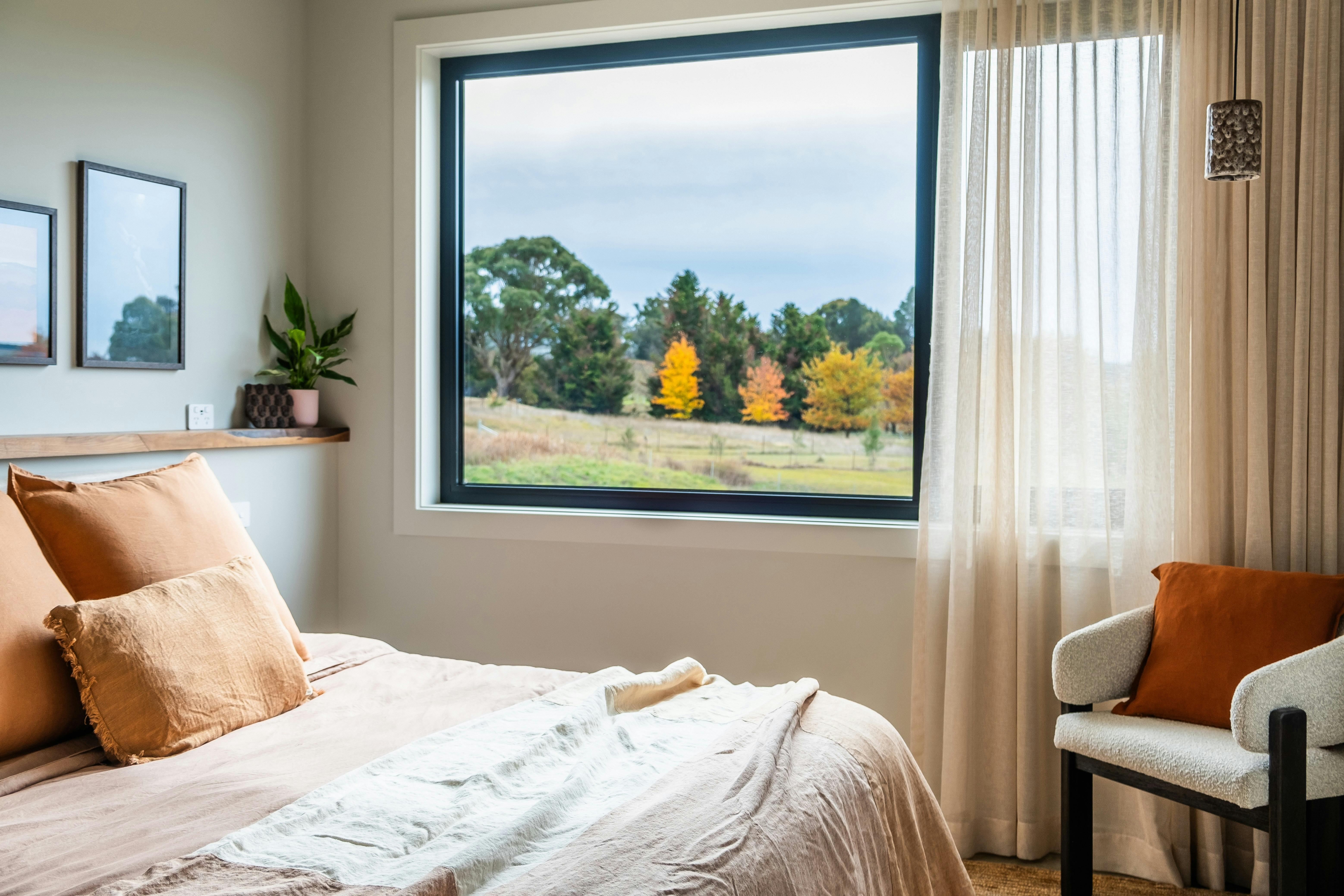 a bed covered in orange linen with an open window and blinds.