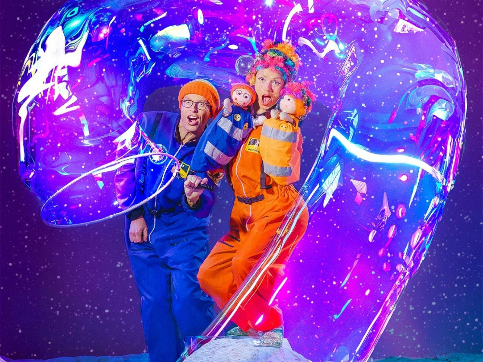 A man & woman with 2 dolls standing in a giant bubble