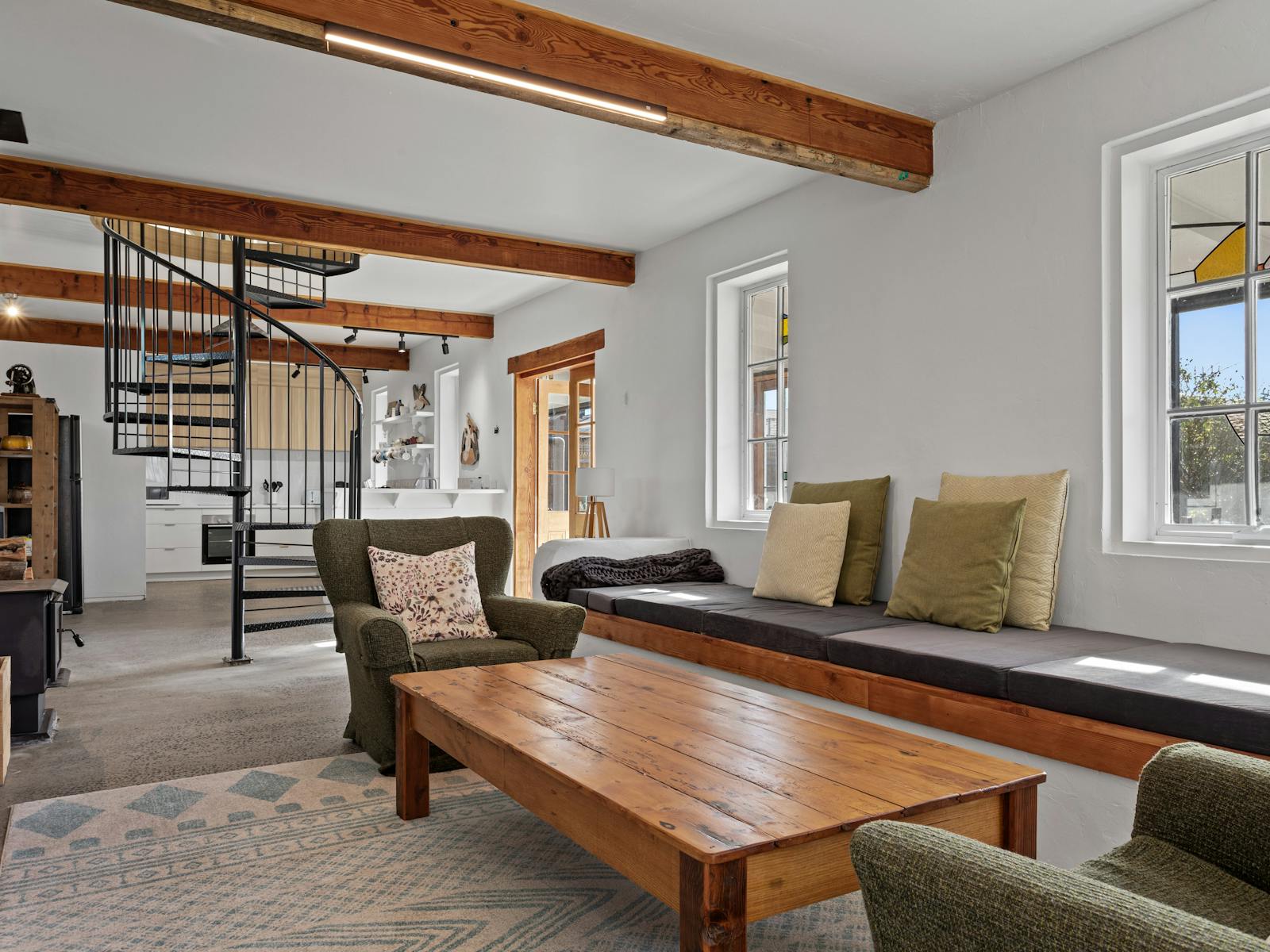 Cottage lounge with spiral staircase, bench seat, armchairs and stained glass windows