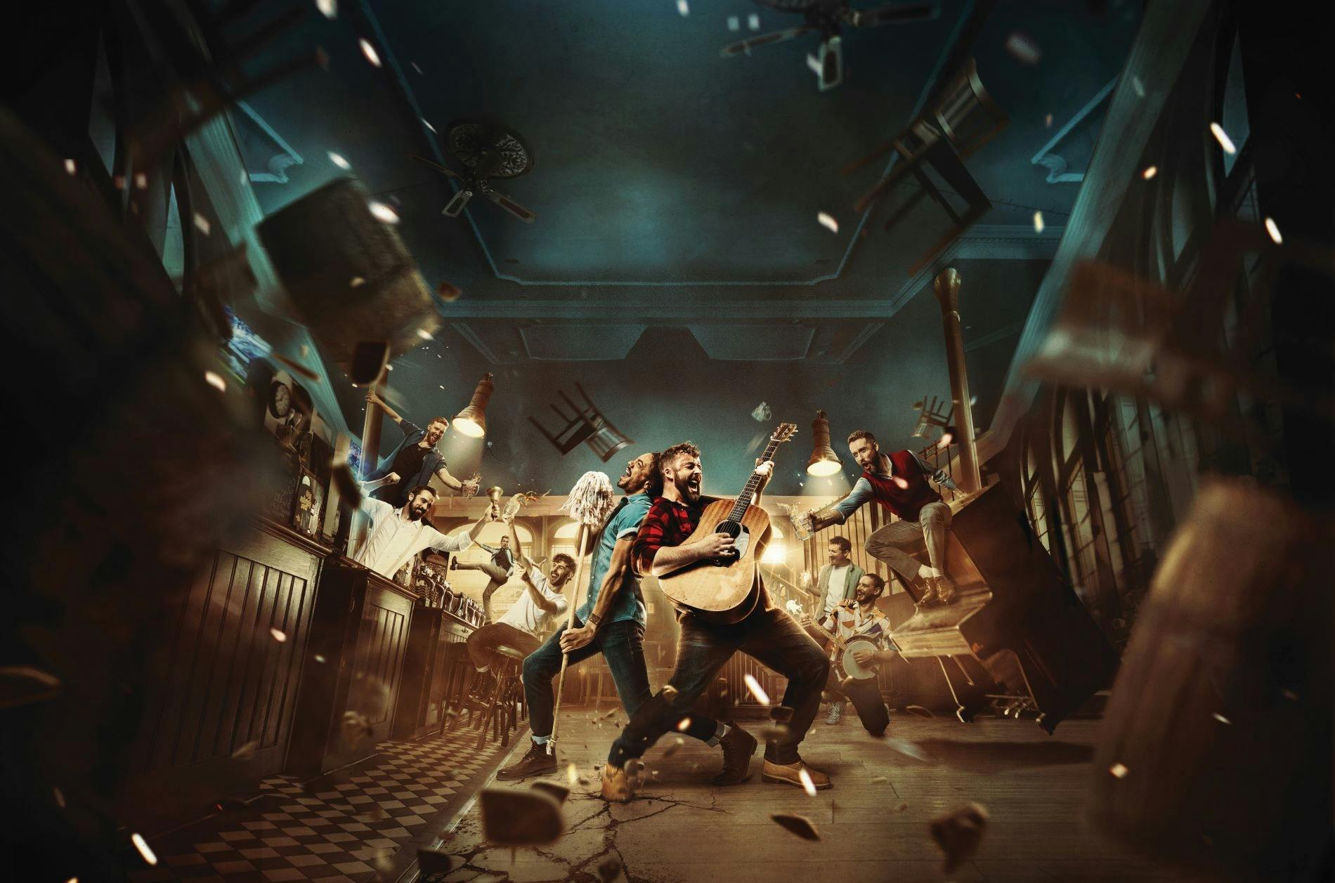 The Choir of Man cast perform with guitars and percussion in a lively pub setting.