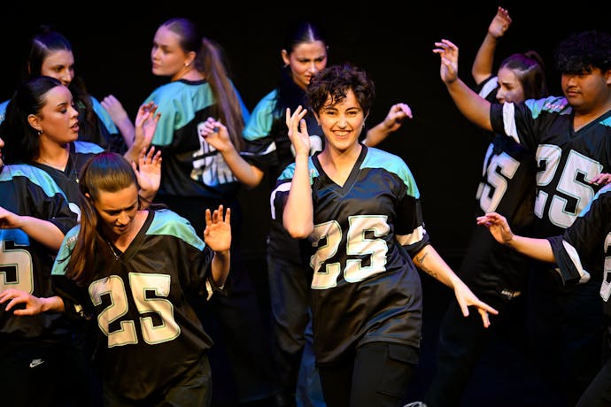 A group of young dancers with the central dancer looking up and smiling. All wearing #25 jersey.