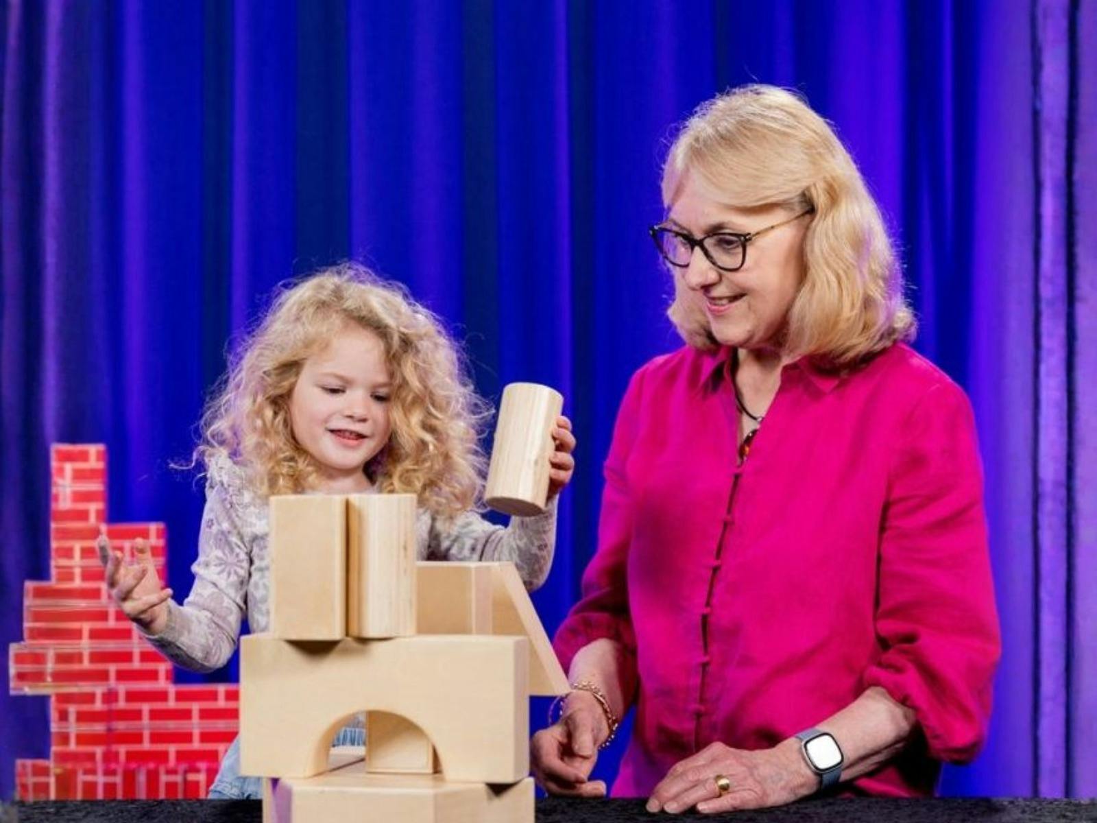 Female child playing with building blocks next to her grandmother