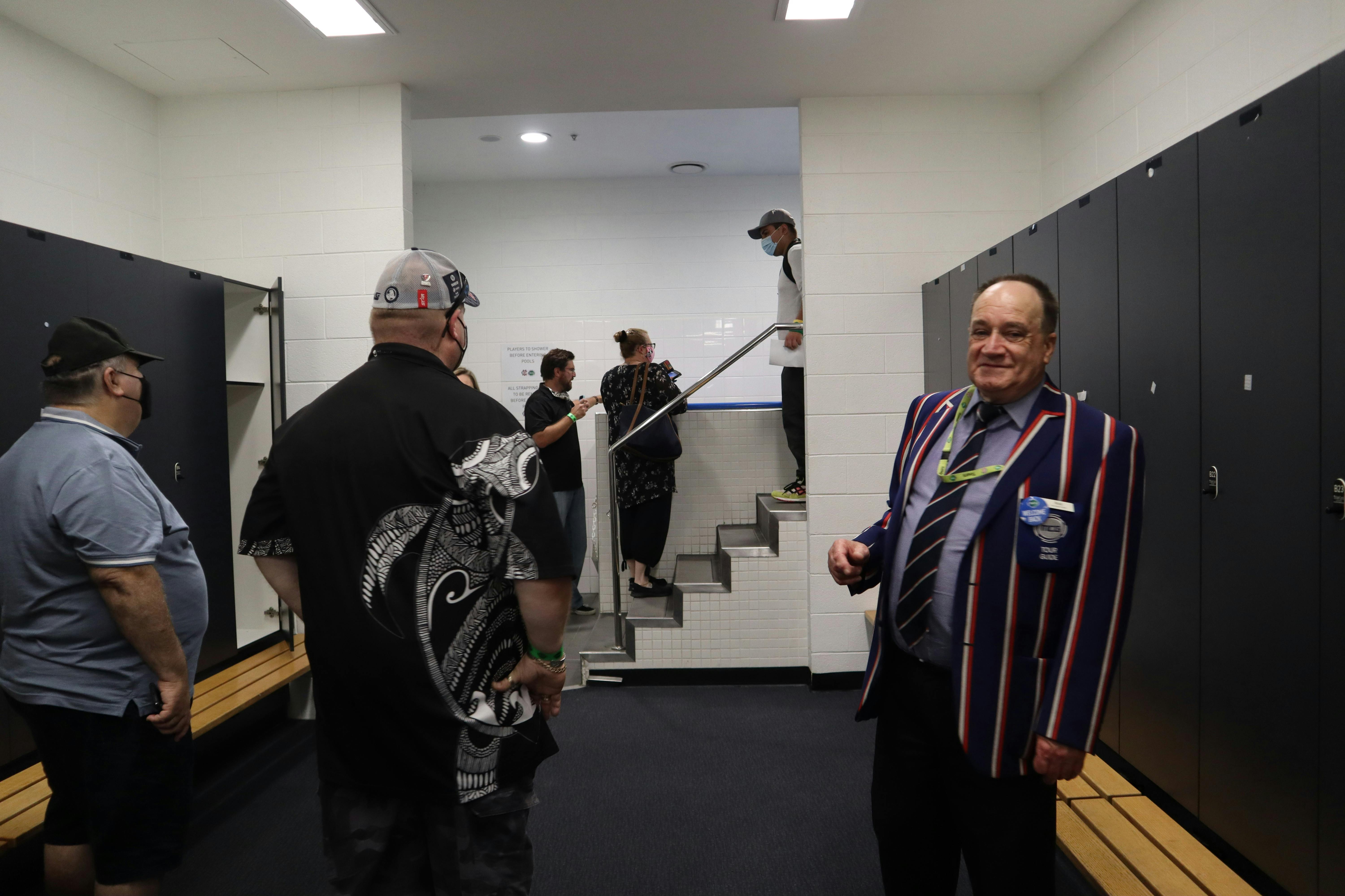 Tour host and guests standing in the locker room at the MCG