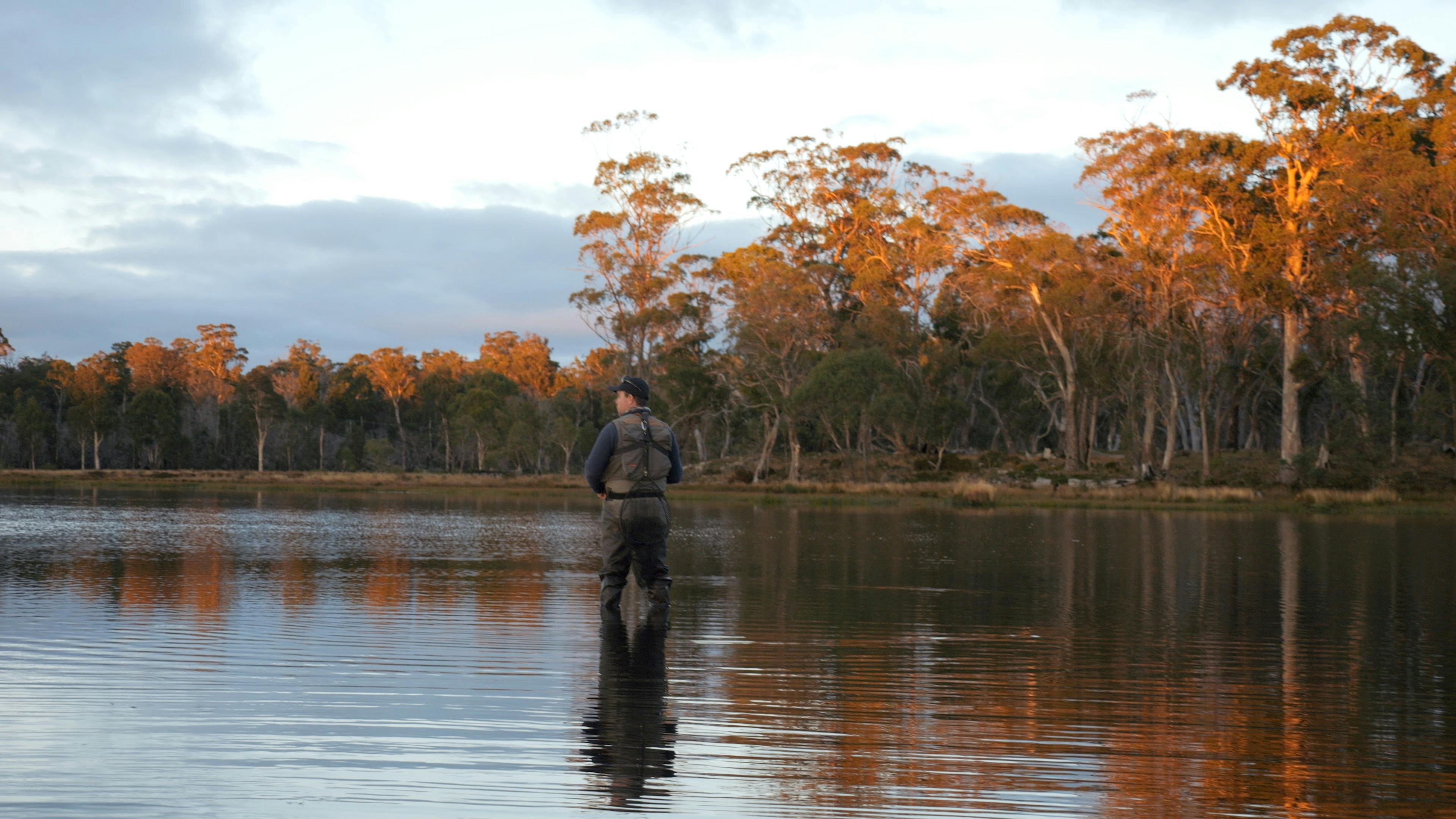 Man standing in water with orange treeline behind