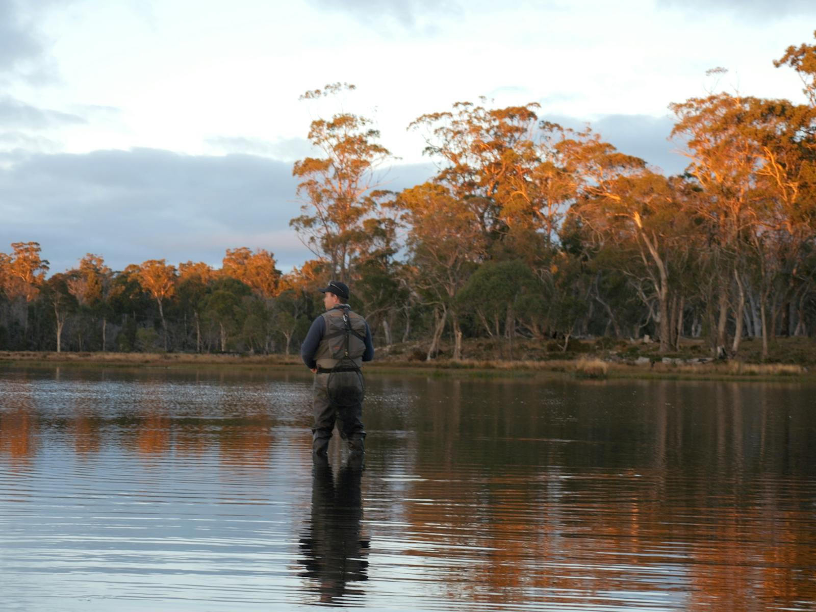 Man standing in water with orange treeline behind