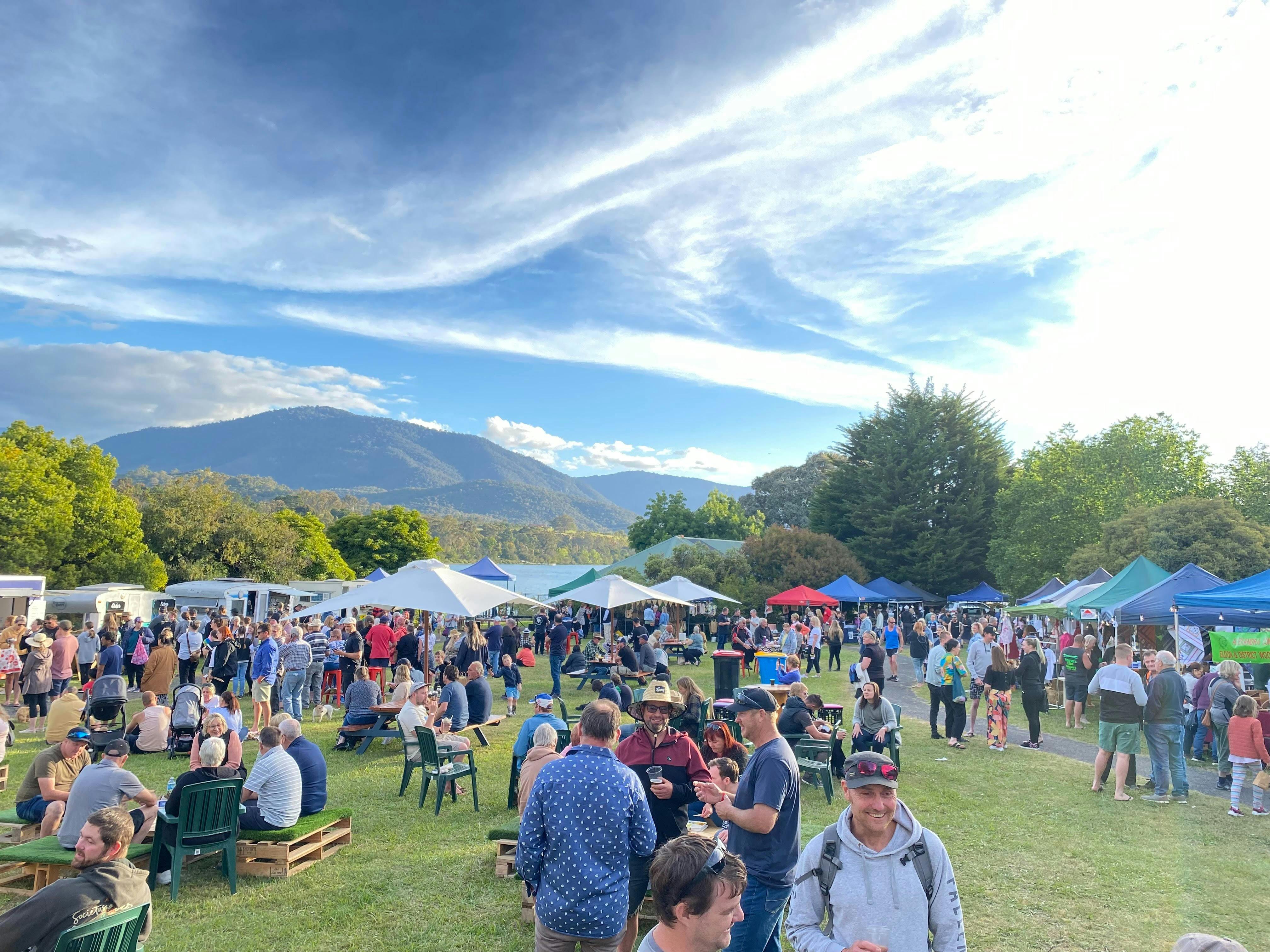 people walking around an open ground with market stalls with the lake and the hills in background