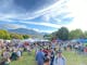 people walking around an open ground with market stalls with the lake and the hills in background