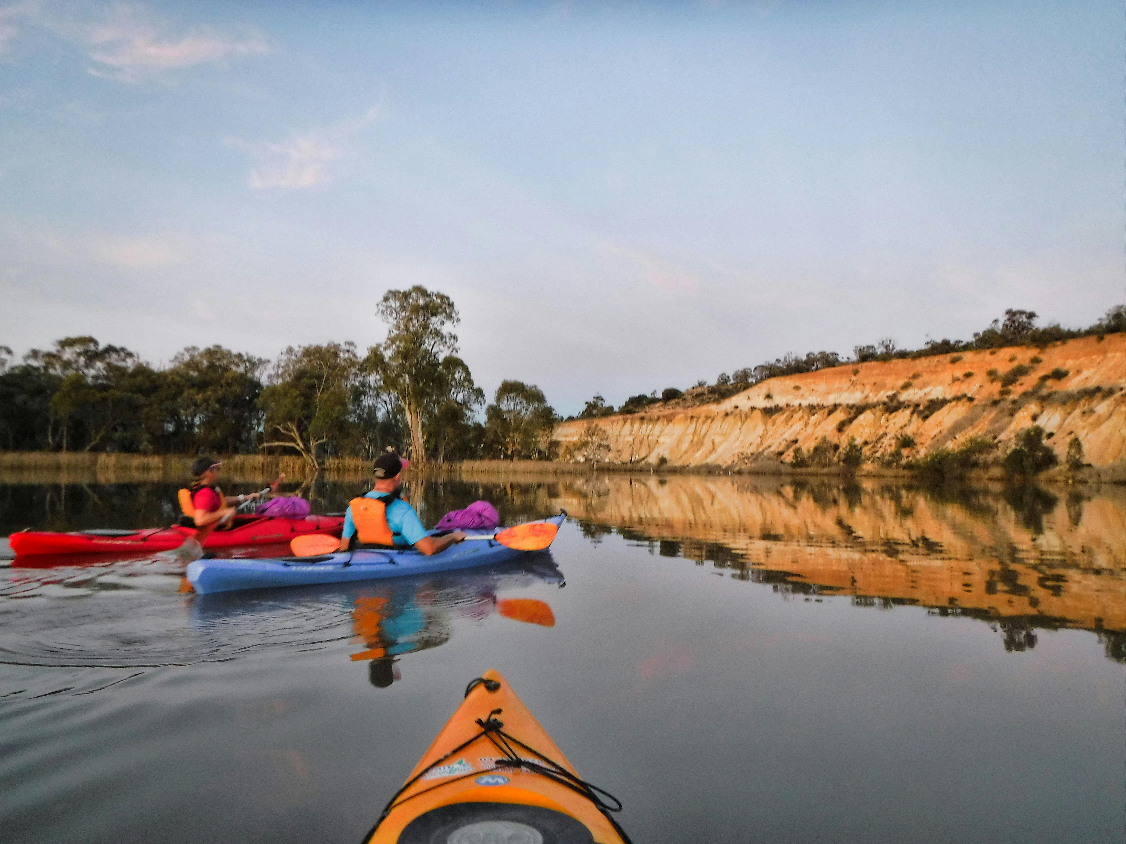 Kayakers in 2 single kayaks paddling on Murray with perfect reflections towards limestone cliffs