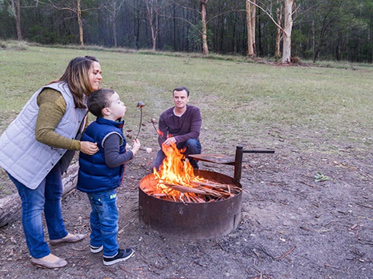 Family roast marshmellows by a fire in the Nikoa section of Euroka campground. Photo: OEH/Simone
