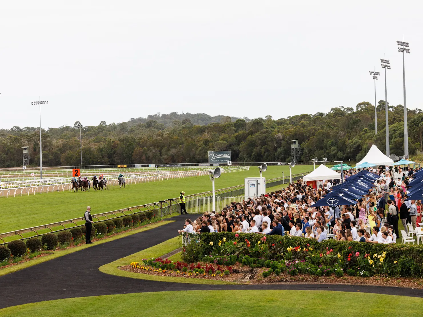 Image overlooking a crowd of people on the lawn watching horse race on the green turf