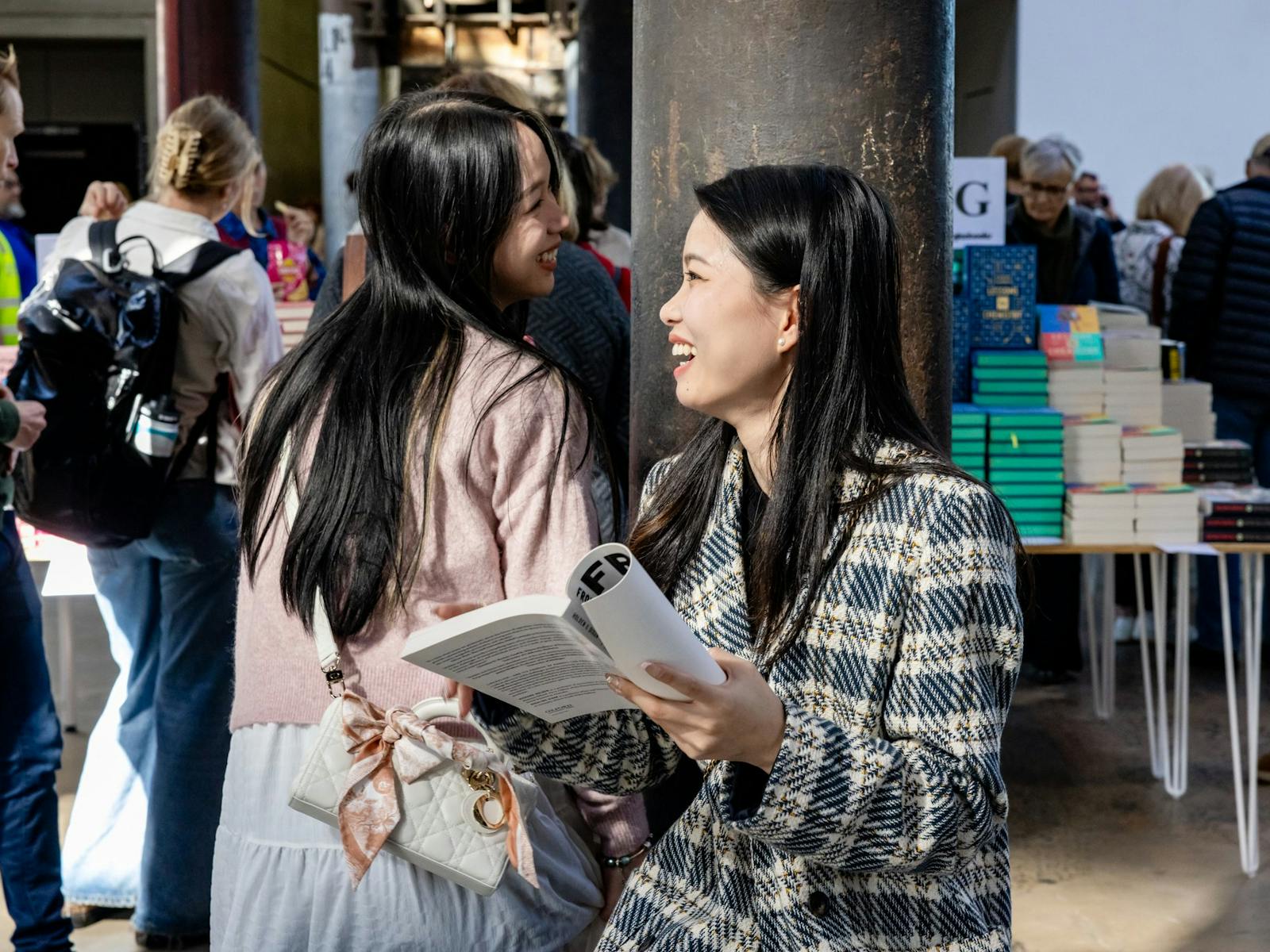 Two women holding a book smile at each other in Carriageworks foyer