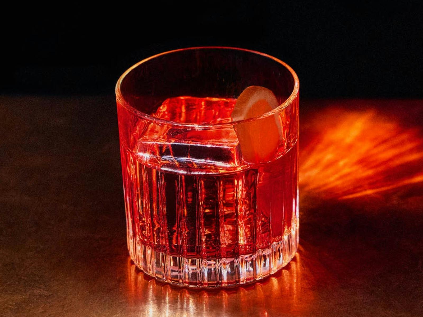 A close-up of a clear, textured glass filled with a Negroni, with a large ice
