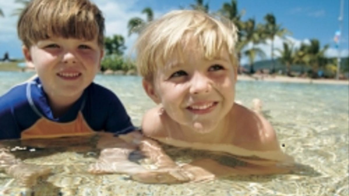 two young boys laying down and smiling in the shallow pool waters