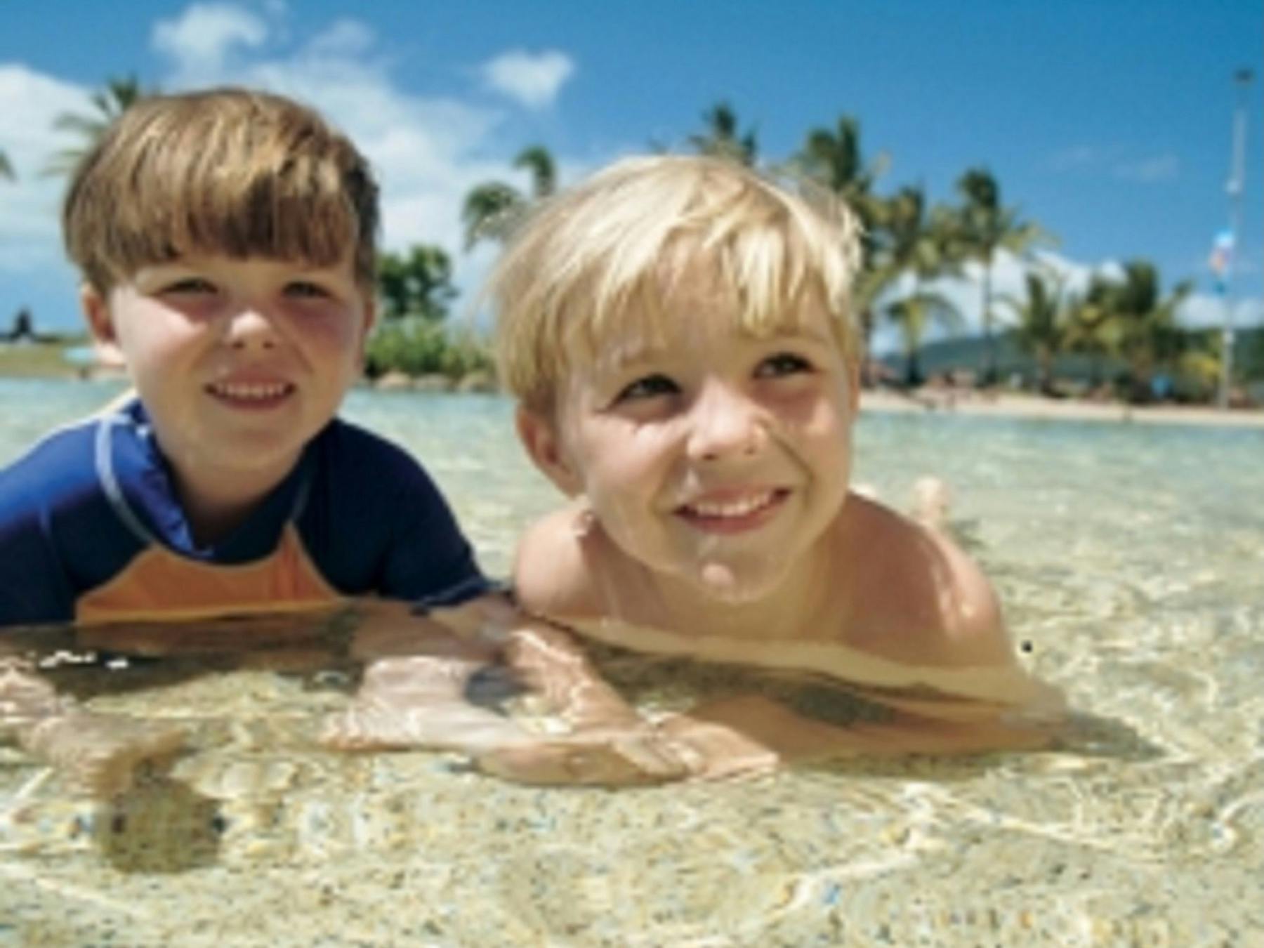 two young boys laying down and smiling in the shallow pool waters