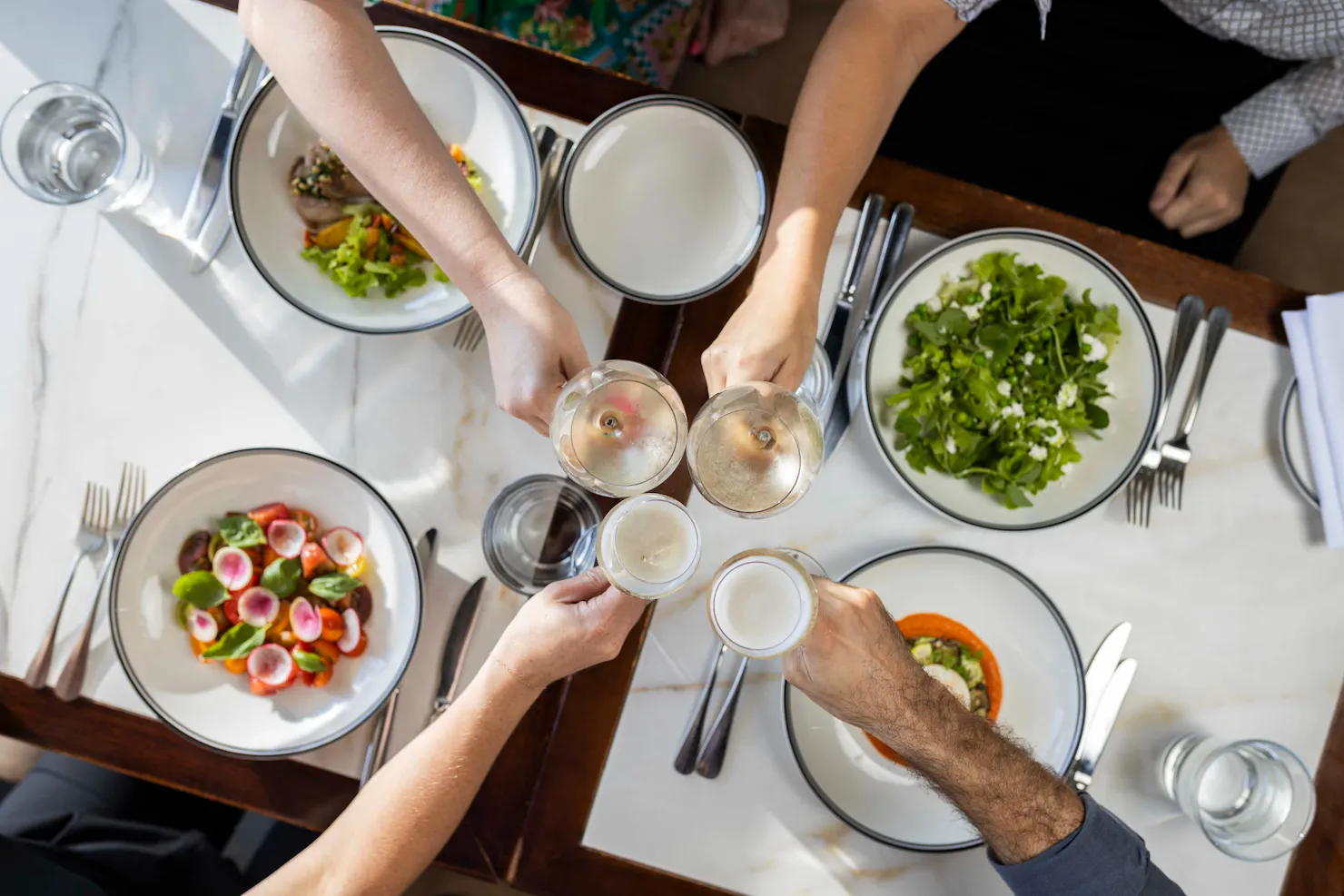 Group dining with hands in doing a cheers over lunch