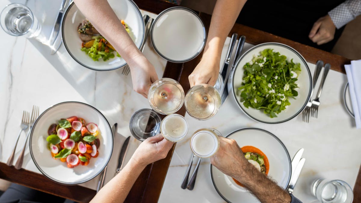 Group dining with hands in doing a cheers over lunch