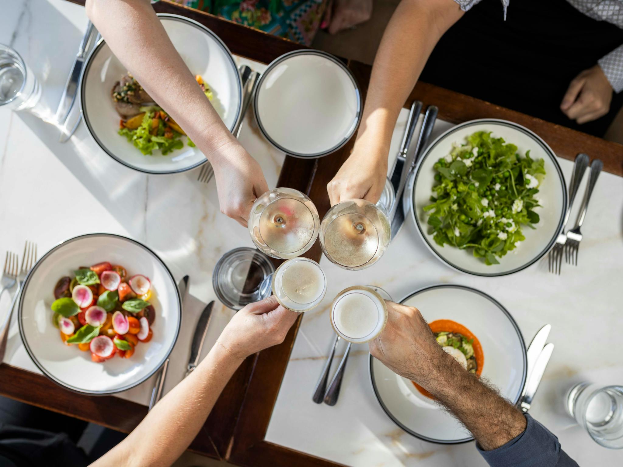 Group dining with hands in doing a cheers over lunch Group dining with hands in doing a cheers over lunch