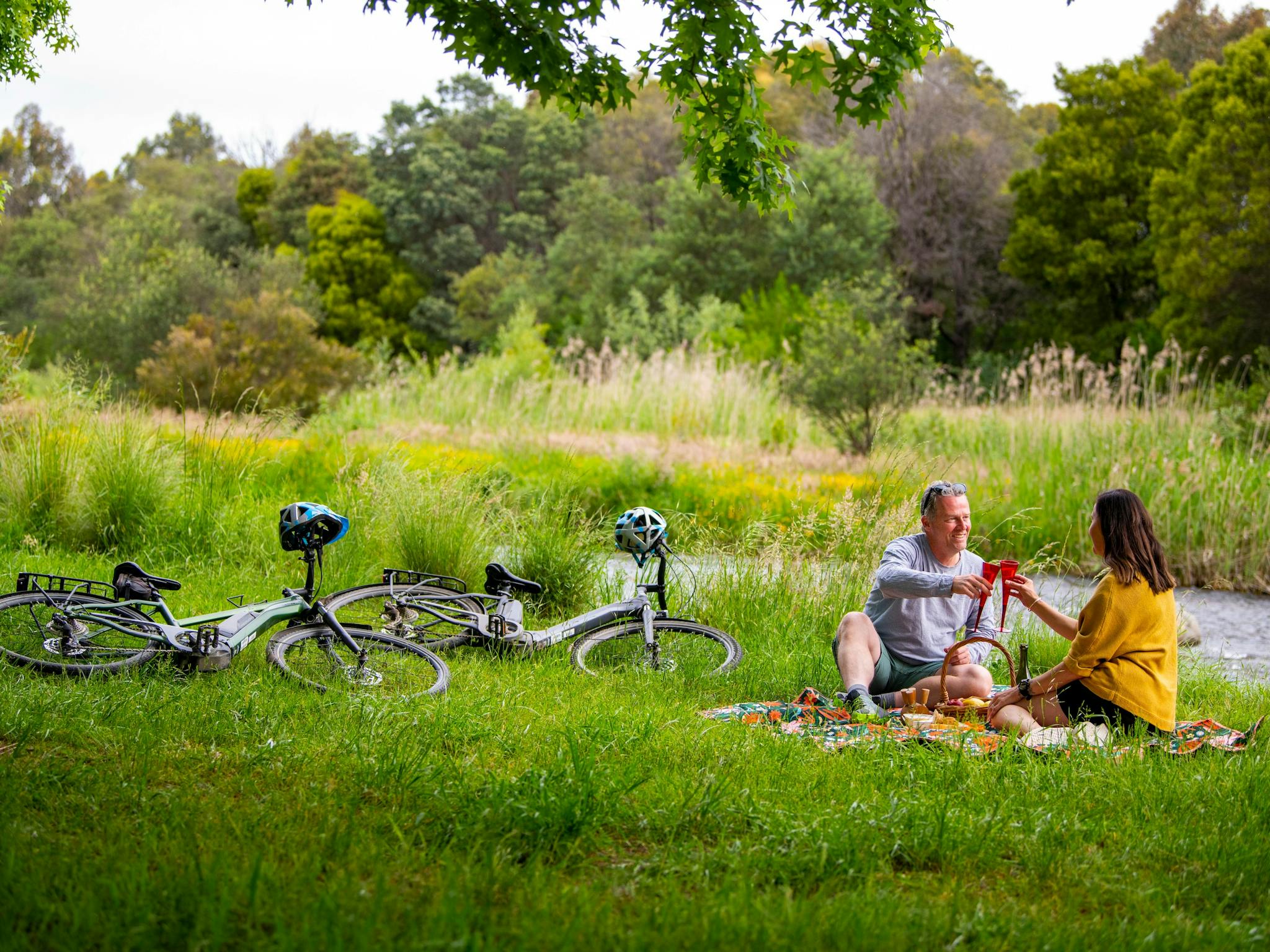 couple enjoy a toast of wine on a picnic by the river after their ebike ride