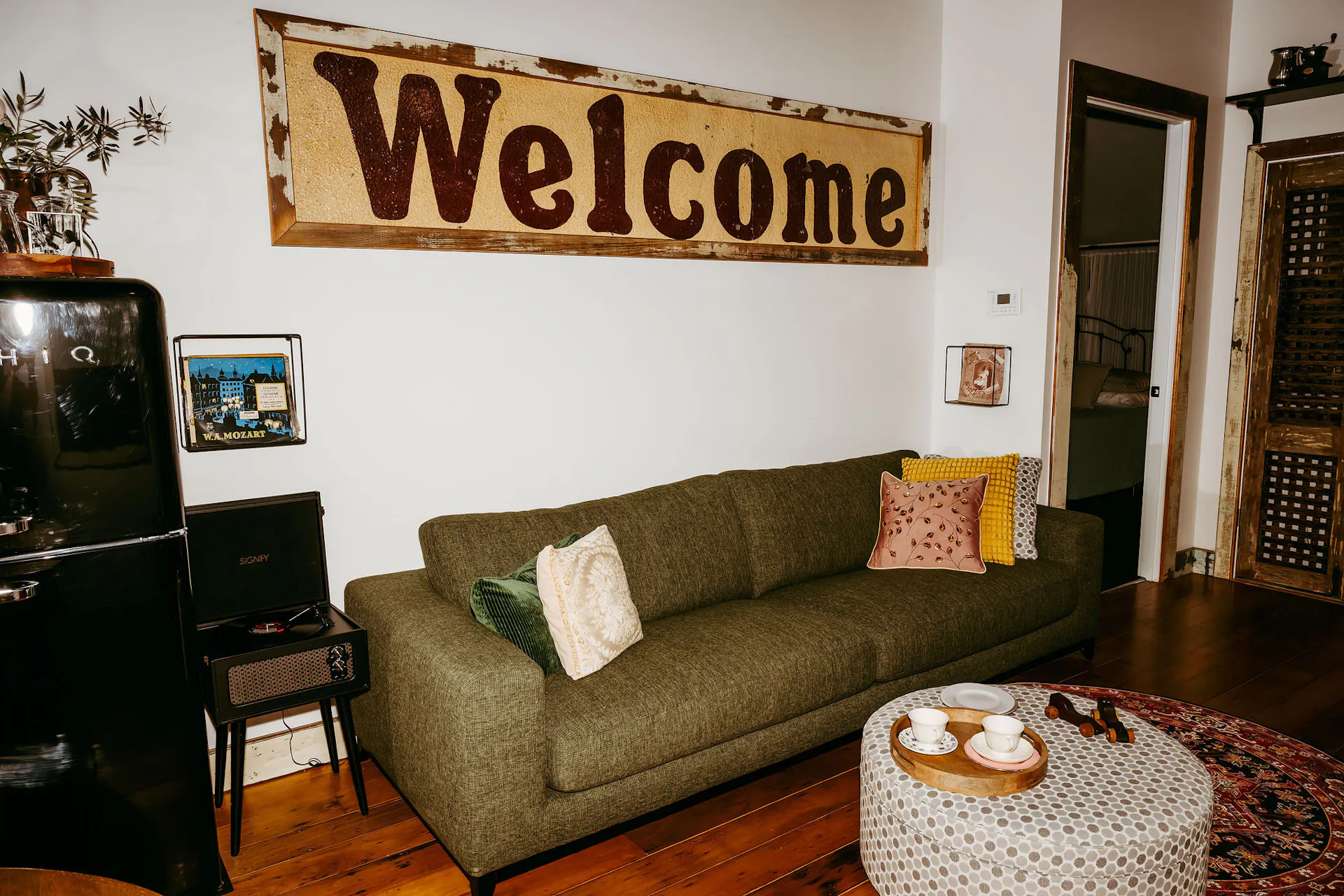 A Welcome sign on the wall as artwork in a lounge area with green large lounge and grey ottoman