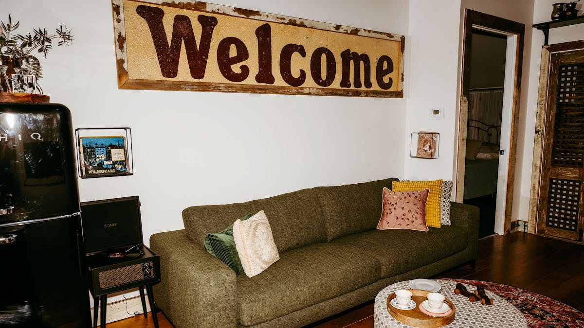 A Welcome sign on the wall as artwork in a lounge area with green large lounge and grey ottoman
