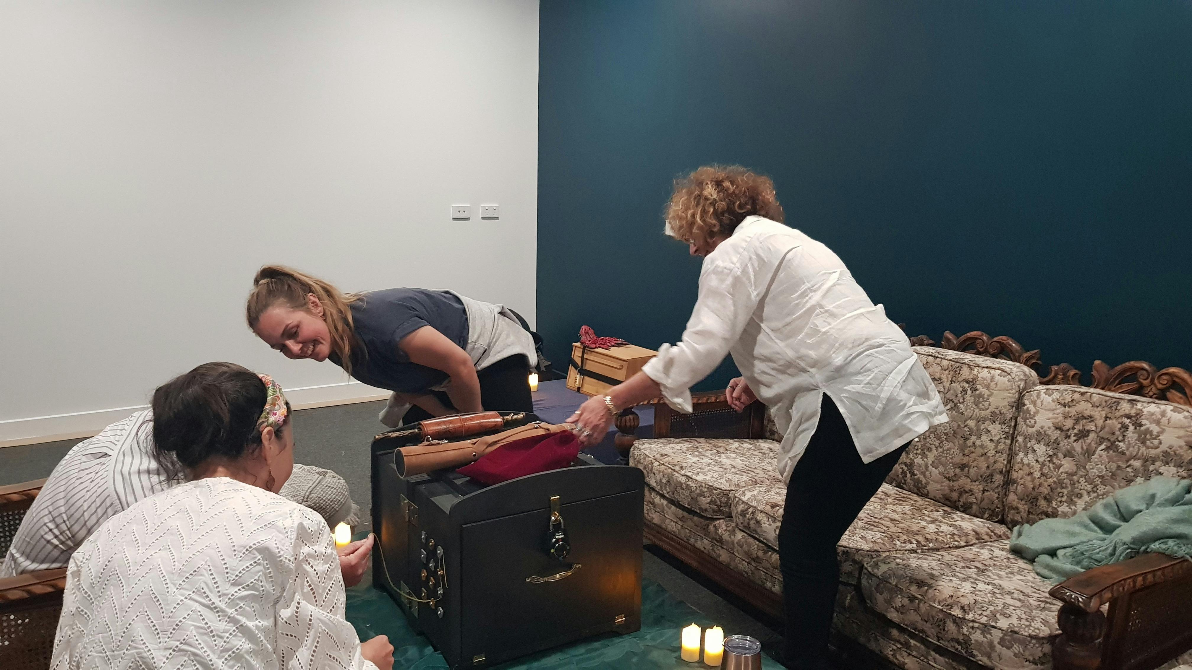 Four people solving puzzles to open a wizard-themed box with numerous buttons and locks.