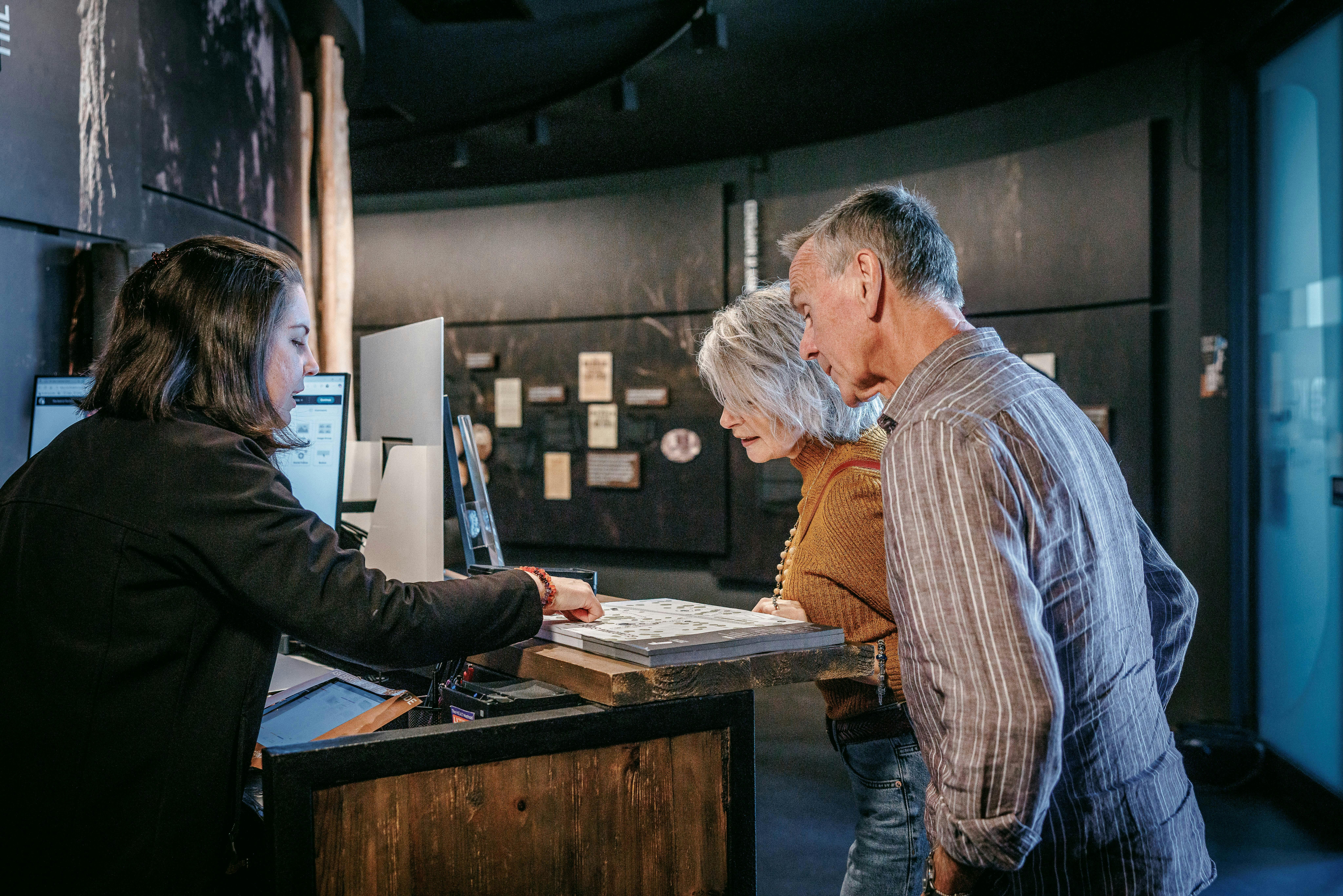 Visitor services staff member assisting two visitors at the Ned Kelly Discovery Hub reception desk.