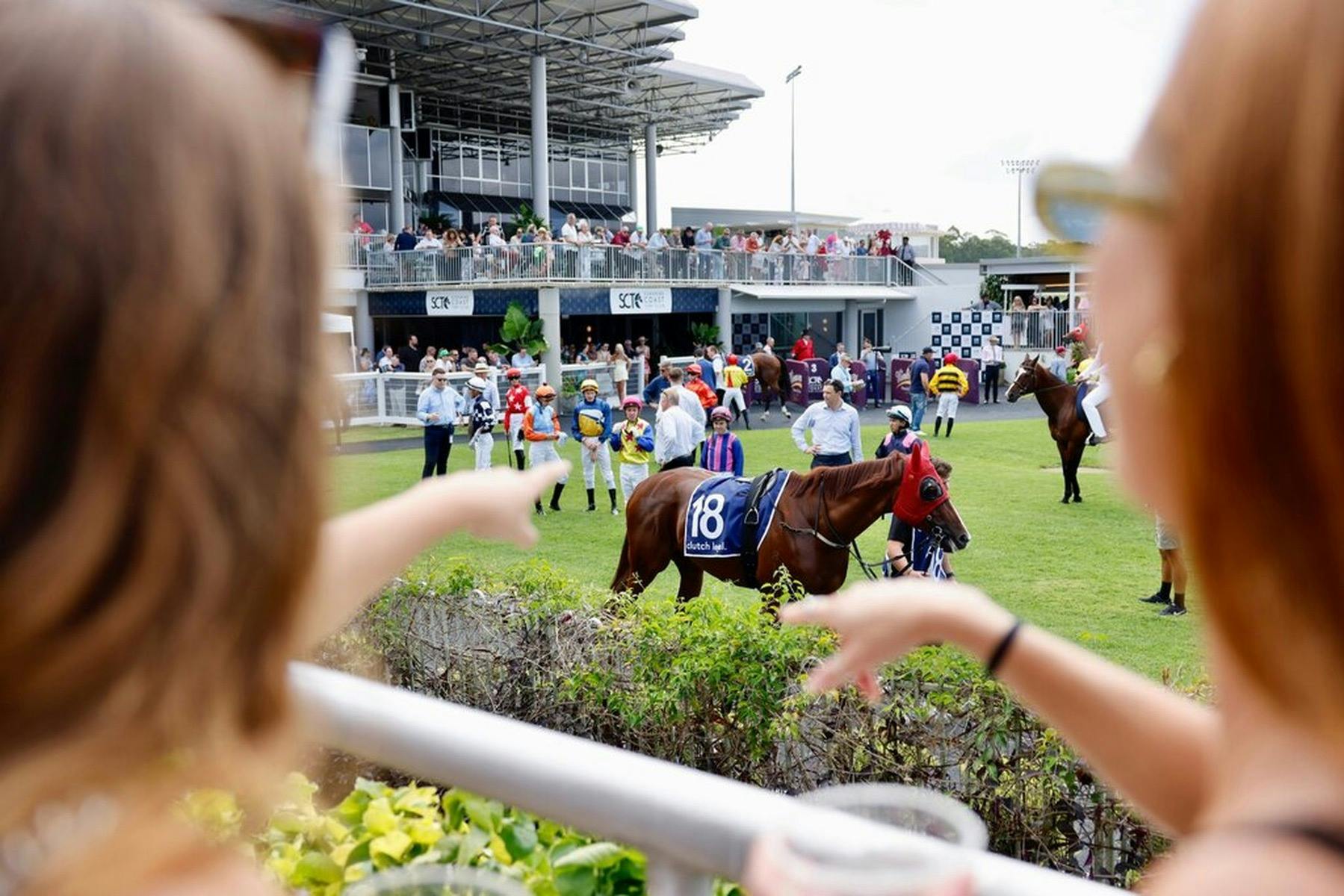 Racegoers gathered at a racecourse to watch live coverage of a major horse race on a big screen.
