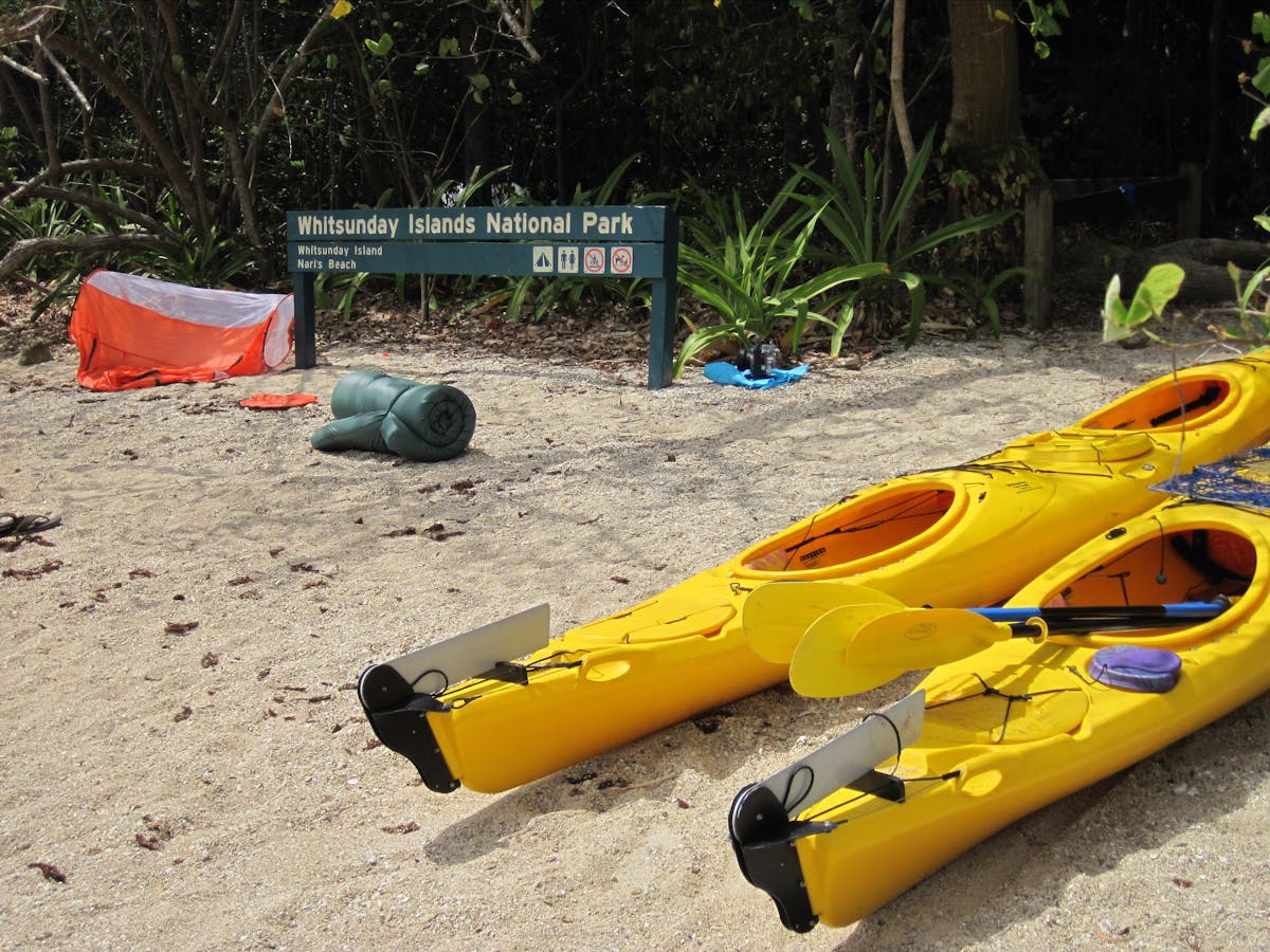 Kayaks on beach near swag, tent and camping area sign. Kayaks on beach near swag, tent and camping area sign.