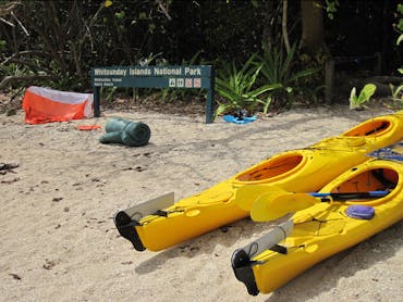 Kayaks on beach near swag, tent and camping area sign. Kayaks on beach near swag, tent and camping area sign.