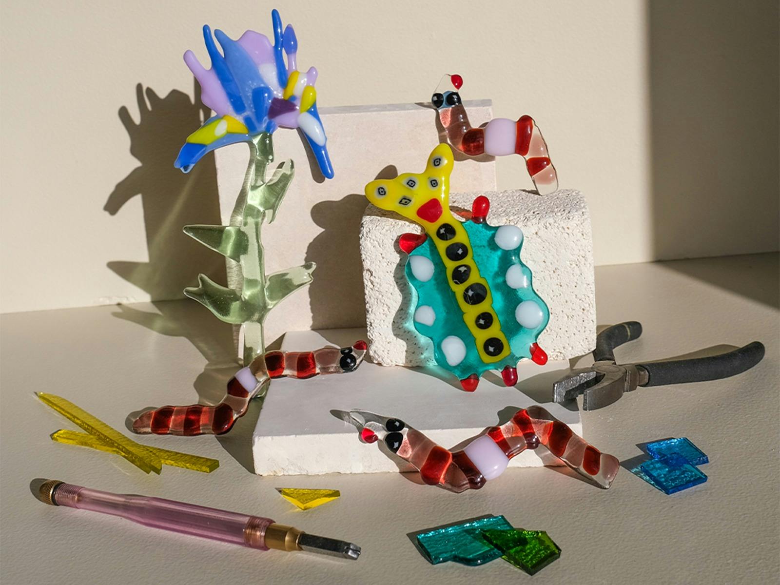Colorful glass flowers, bugs and worms climbing over kiln blocks, surrounded by glass shards and too