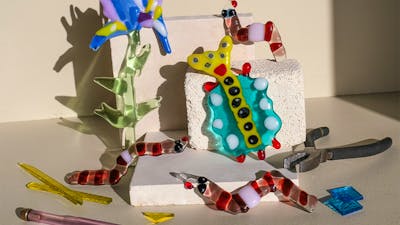 Colorful glass flowers, bugs and worms climbing over kiln blocks, surrounded by glass shards and too