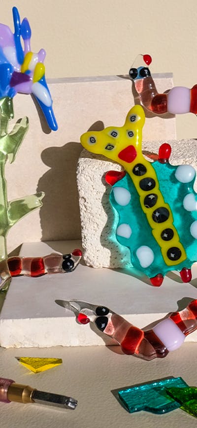 Colorful glass flowers, bugs and worms climbing over kiln blocks, surrounded by glass shards and too