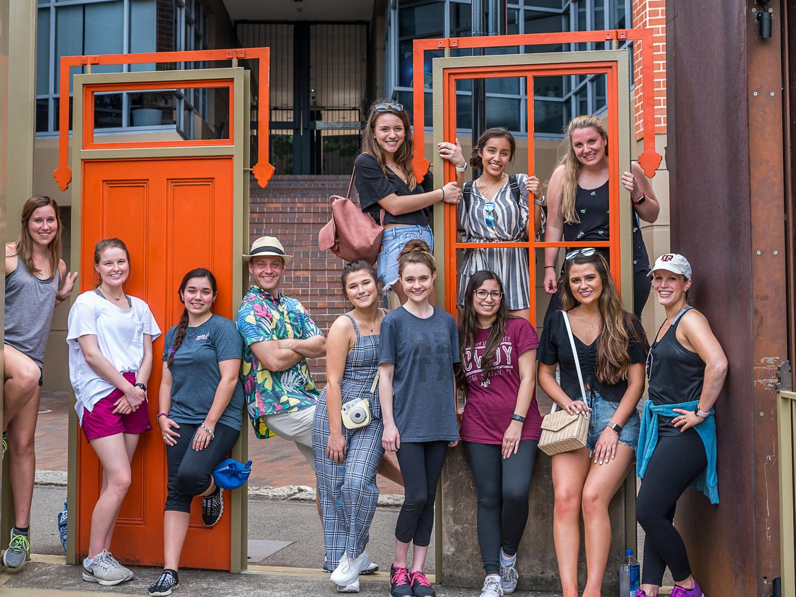 Group of young ladies with teachers stand casually at a red door artwork