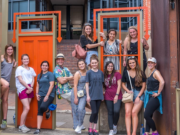 Group of young ladies with teachers stand casually at a red door artwork