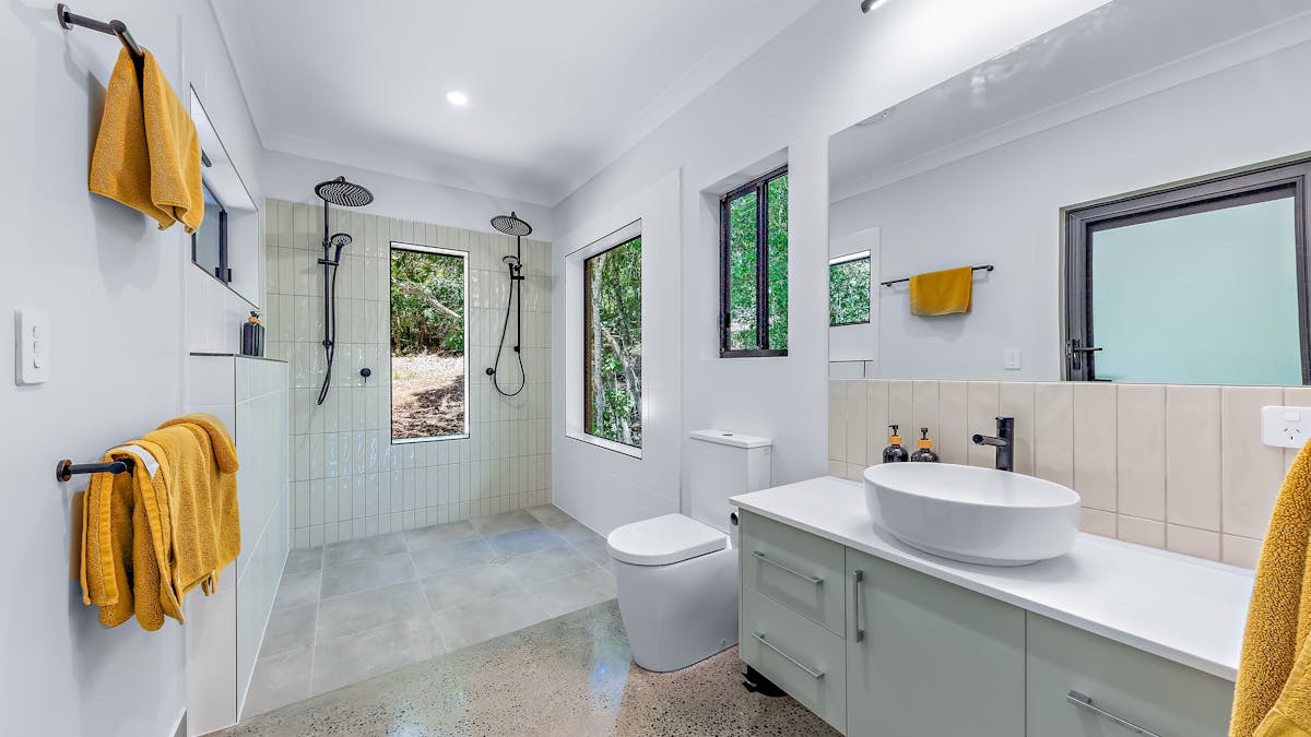 Bathroom with double shower heads, toilet and vanity.  Views to outside.